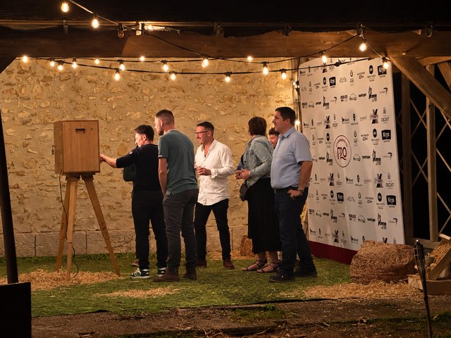Un groupe d’invités devant une borne photo sous des guirlandes dans un décor champêtre.