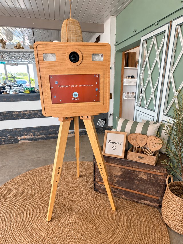 Vue rapprochée d’un photobooth en bois clair avec écran tactile et panier d’accessoires.