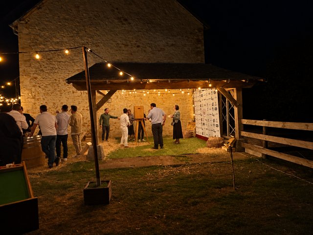 Espace photobooth sous un abri en bois, guirlandes lumineuses et invités à la nuit tombée.