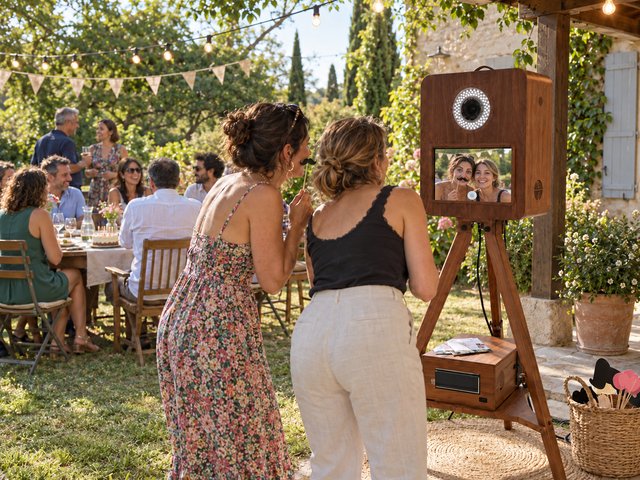 Deux invitées utilisent un photobooth en bois lors d’une réception champêtre au jardin.
