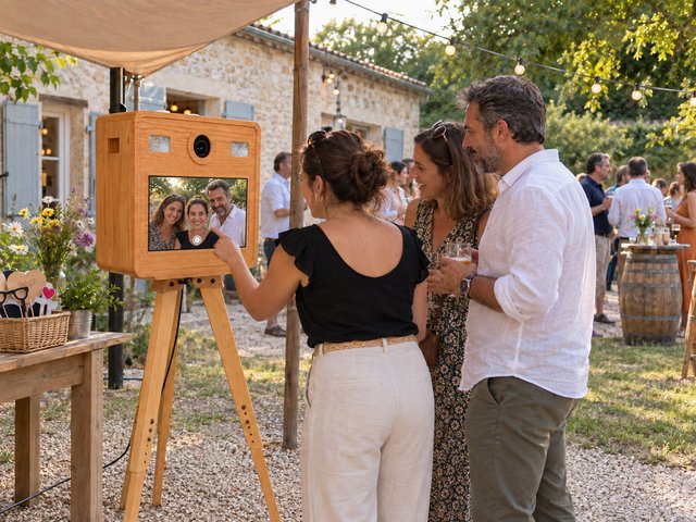 Trois invités prennent une photo avec une borne en bois lors d’une réception extérieure.