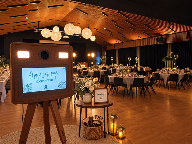 Borne photo en bois et coin accessoires devant les tables dressées d’une salle de réception.